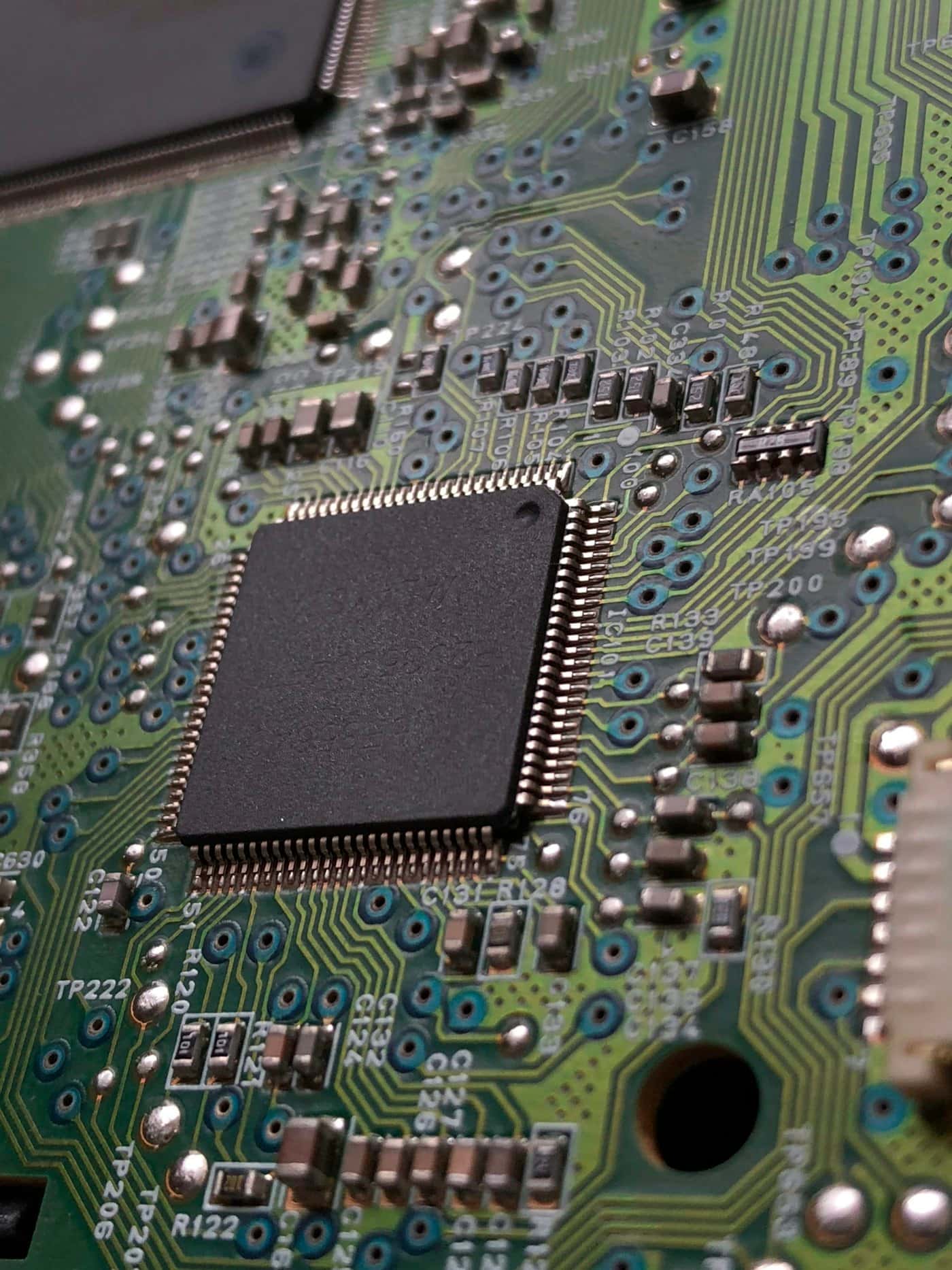 Close-up of a fine-pitch QFP chip soldered onto a green circuit board
